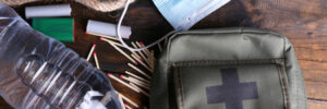 Survival kit items on a wooden surface: face mask, water bottle, rope, matches, lighter, and first aid pouch.