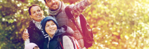 A family of four dressed in autumn clothes stands outdoors, with the father pointing at something in the distance.