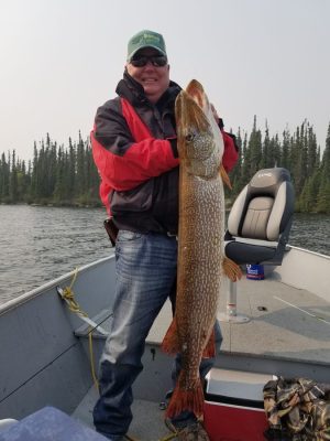 Person on a boat holding a large fish, with a forested shoreline in the background.