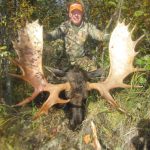 Hunter in camouflage poses with a large moose and massive antlers in a forested area. Date stamp on image: 09/21/2010.