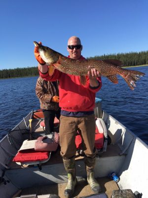 Person in a boat holding a large fish, with another person in the background. The scene is set on a sunny day on a lake.