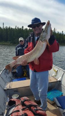 Two people in a boat on a lake, with one person holding a large fish and smiling at the camera.