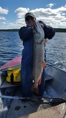Person in a boat holding a large fish vertically against their body, with water and cloudy sky in the background.