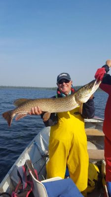 Person in a yellow suit holding a large fish on a boat, with water and trees in the background.