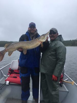 Two people on a boat holding a large fish, posing for a photo on a cloudy day.