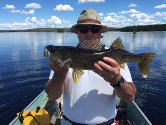 Person in a boat holding a large fish against a backdrop of a calm lake and cloudy sky.