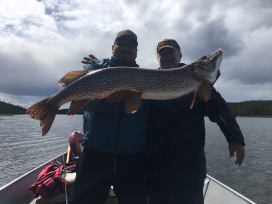 Two people on a boat hold a large fish together against a cloudy sky.