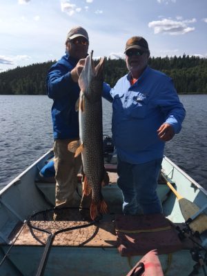 Two men on a boat holding a large fish. One man supports the fish's mouth while the other stands beside him.