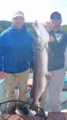 Two men on a boat hold up a large fish with a fishing net nearby.