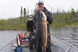 Two people in a boat; one holds a large fish, while the other looks down and handles fishing equipment.