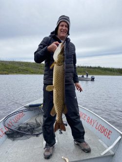 Person standing on a boat holding a large fish, with fishing equipment visible and another boat in the background.