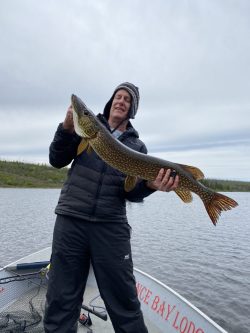 Person in a boat holding a large fish with both hands, overcast sky and water in the background.