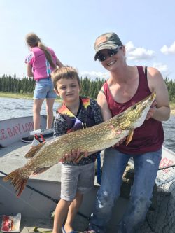 Woman and boy on a boat hold a large fish together; another girl stands at the boat's edge facing away.