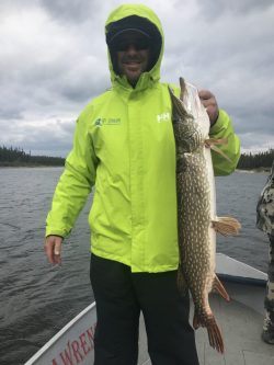 Person in a bright green jacket holding a large fish on a boat in a lake with cloudy skies.