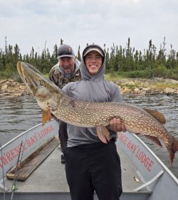 Two people on a boat; the person in front holds a large fish while the other stands behind, smiling.