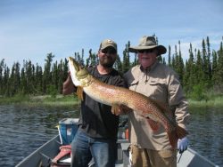 Two people on a boat holding a large fish with trees and water in the background.
