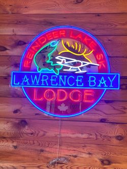 Neon sign on wood wall reading "Lawrence Bay Lodge, Reindeer Lake SK," with images of a fish and antlers.