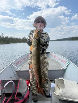 Person in camouflage clothing holds a large fish on a boat with "Lawrence Bay Lodge" written on the boat's side.