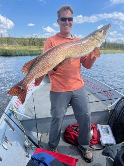 A man standing on a boat holds a large fish with both hands, smiling at the camera.