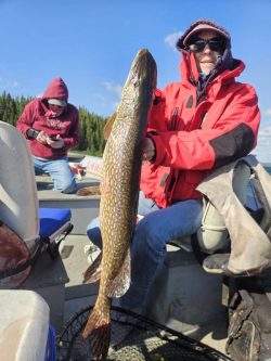 Person in a red jacket holding a large fish on a boat, with another person sitting in the background.