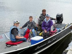 Four people, including three children and one adult, sit in a small motorboat on calm water, ready for fishing.